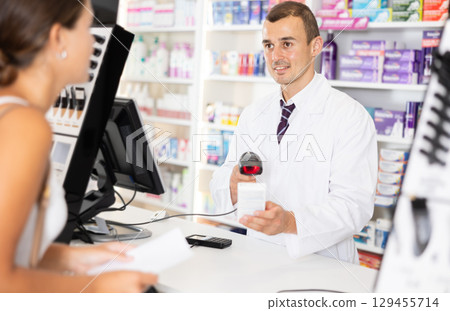 Young male pharmacist serving client buying medicament in drugstore Young male pharmacist serving client buying medicament in drugstore 129455714