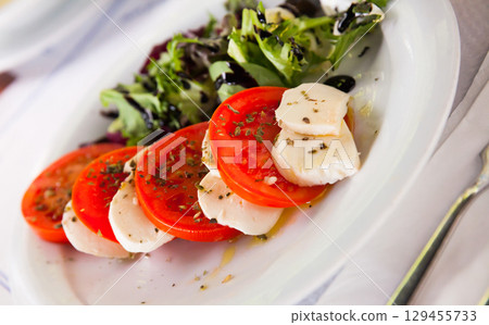 Caprese salad with fresh tomatoes, mozzarella cheese and basilic herb, dish of Italian cuisine 129455733