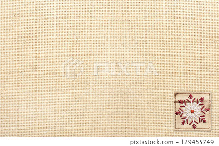 Horizontal Christmas background with beige canvas texture and felt snowflake. Holiday backdrop for scrapbooking with linen fabric texture and decorative snowflake. Copy space for text Horizontal Christmas background with beige canvas texture and felt snowflake. Holiday backdrop for scrapbooking with linen fabric texture and decorative snowflake. Copy space for text 129455749