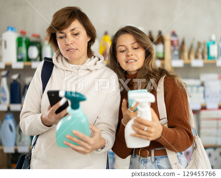 Two women checking expiration date of spray glass cleaner using her smartphone in supermarket 129455766