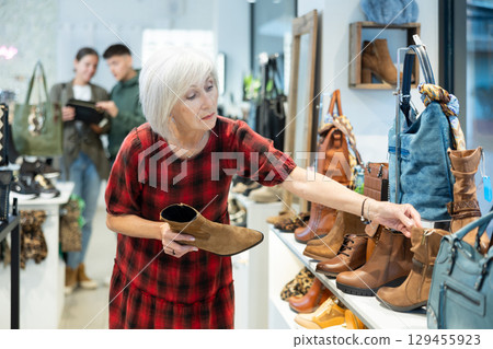 Contemplative elderly woman choosing demi-season boots in shoe store 129455923