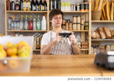 Young male seller with phone in grocery store 129456069
