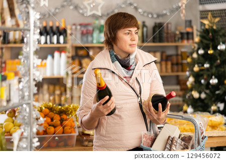 Woman with shopping basket buying bottle of wine for christmas celebration Woman with shopping basket buying bottle of wine for christmas celebration 129456072