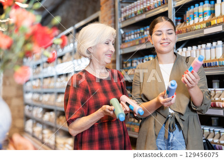 Two women consult with each other what pigment or acrylic varnish to choose for their future clay or ceramic dishes in specialized store Two women consult with each other what pigment or acrylic varnish to choose for their future clay or ceramic dishes in specialized store 129456075
