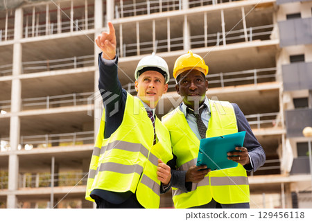 Foreman showing builder something at the construction site by pointing hand Foreman showing builder something at the construction site by pointing hand 129456118