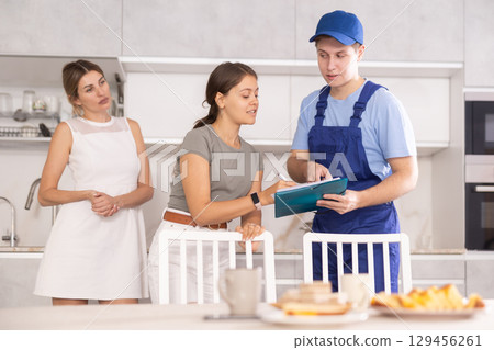 Guy employee of repair team in blue overalls submits to female client document on payment Guy employee of repair team in blue overalls submits to female client document on payment 129456261