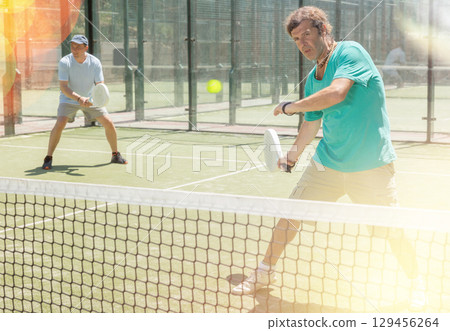 Men play padel on an outdoor tennis court. Hitting the ball with racket 129456264