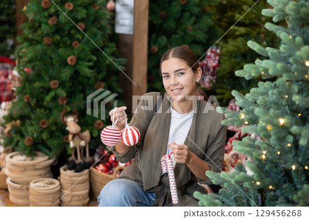 Girl buyer considers New Year and Christmas decorations ornaments for Christmas tree 129456268