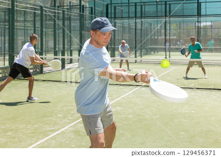 Men play padel on an outdoor tennis court. Hitting the ball with racket Men play padel on an outdoor tennis court. Hitting the ball with racket 129456371