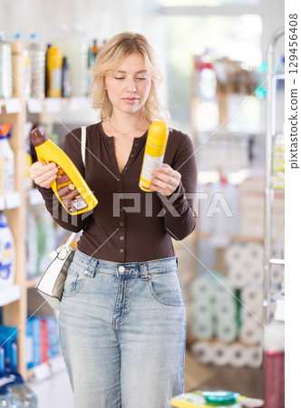 Focused interested young woman carefully choosing parquet and wood cleaner in hardware department of supermarket 129456408