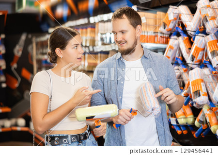 Married couple choose paint brush and paint roller together for their home renovation at hardware store 129456441