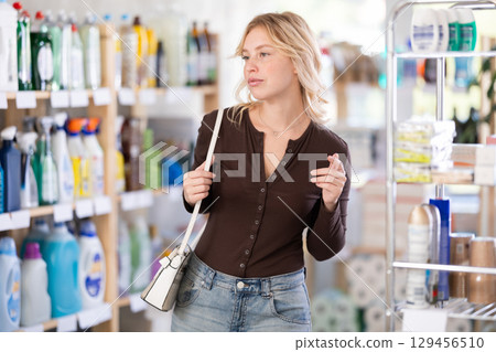 Young woman looking for something on shelf of showcase, reviews assortment in household shop 129456510