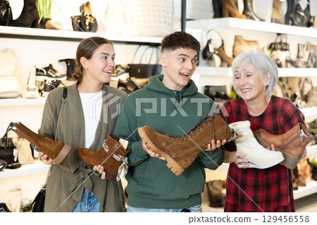 Mature woman sales consultant helps couple customers decide on choice of model of winter shoes 129456558