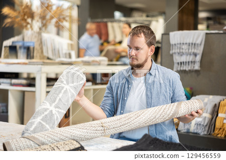 Male shopper carefully choose soft carpet in hardware store Male shopper carefully choose soft carpet in hardware store 129456559