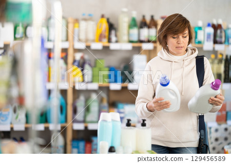 Adult woman housewife purchases household chemicals in store, choose liquid detergent Adult woman housewife purchases household chemicals in store, choose liquid detergent 129456589