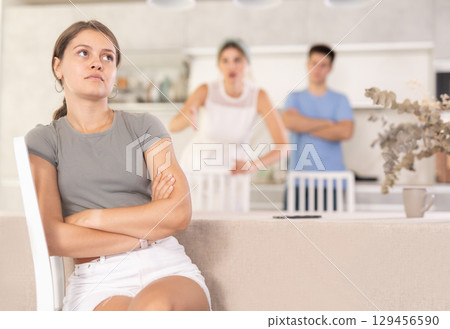 Mother-in-law and son scold young daughter-in-law in home kitchen 129456590