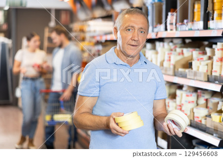 Senior man buy sticky adhesive tape in construction store for carrying out internal finishing work 129456608