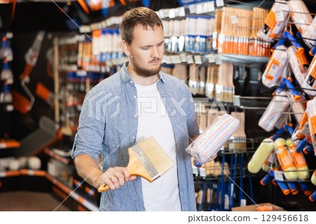 Young man choosing paint rollers and brushes Young man choosing paint rollers and brushes 129456618