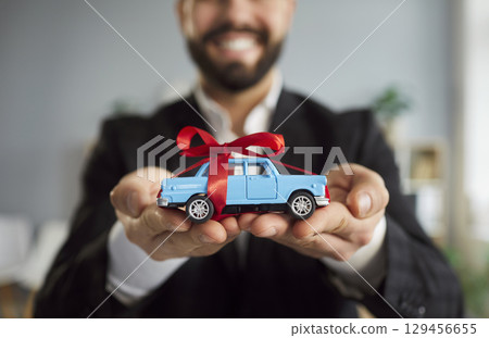 Close-Up Of Man Holding Toy Car With Red Ribbon 129456655