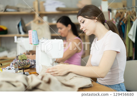 Two women tailor sews clothes in sewing machine 129456680