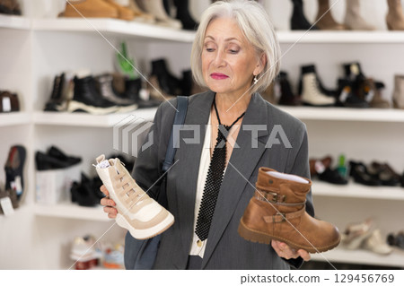 Mature woman takes samples from showcase and examines shoes 129456769