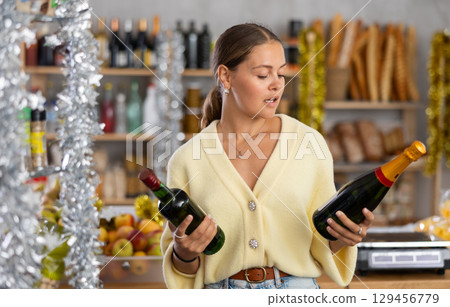 On New Years Eve, girl shopper compare wine and champagne, buys alcoholic beverages 129456779