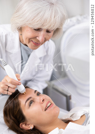 Young woman having face radiolifting procedure made by doctor 129456812