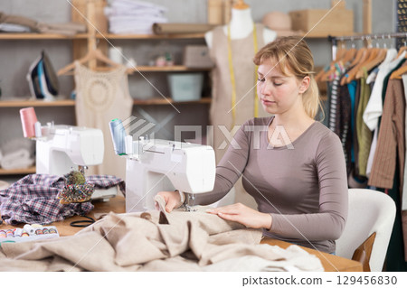 Young female dressmaker working with sewing-machine in tailor's workshop 129456830
