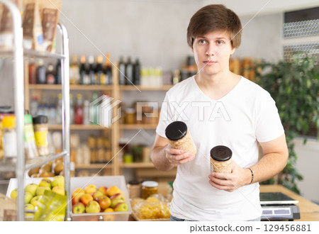 Young man store visitor chooses can of beans, hold and view glass jar package. 129456881