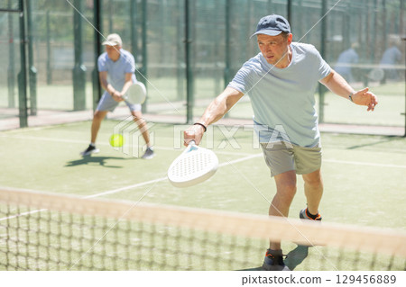 Elderly and adult men playing doubles padel 129456889