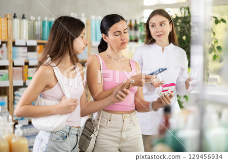 Mother and daughter scan paracetamol qr code with pharmacist 129456934