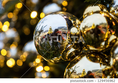 Reflection of couple in golden Christmas bauble with festive lights in background 129456962