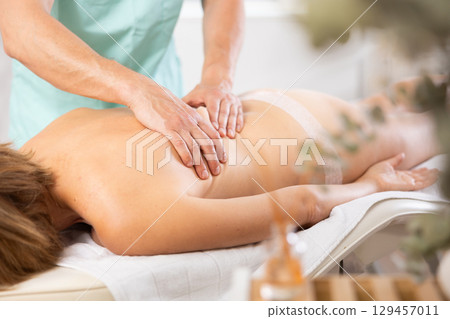 Woman dressed in tango panties receives massage of shoulder area, close-up, male masseur 129457011