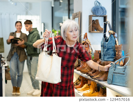 Elderly woman looking at models of womens handbags in trendy store Elderly woman looking at models of womens handbags in trendy store 129457016