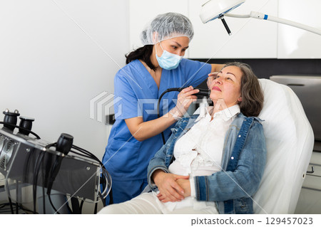 Aged female client receiving face skin rf lifting procedure 129457023