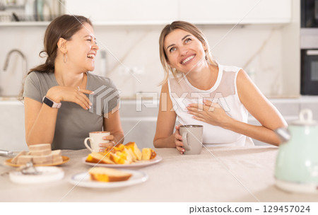 Two women having fun chatting and eating cupcake or pie in home kitchen Two women having fun chatting and eating cupcake or pie in home kitchen 129457024