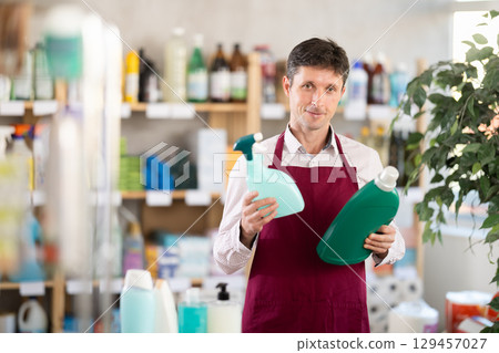 Middle-aged salesman offering detergent and spray in retail store 129457027