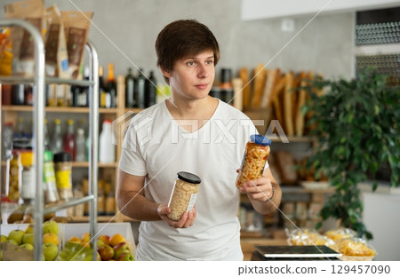 Young man store visitor chooses can of beans, hold and view glass jar package. Young man store visitor chooses can of beans, hold and view glass jar package. 129457090