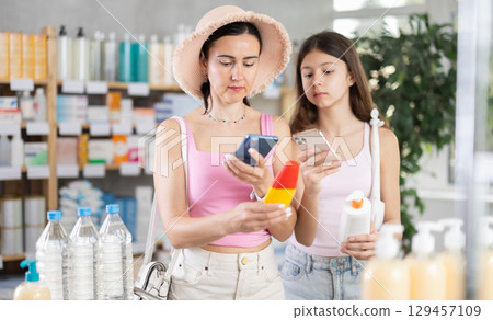 Mom and daughter scanning barcode on sunscreen in chemist's shop Mom and daughter scanning barcode on sunscreen in chemist's shop 129457109