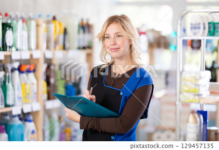 Woman seller, with papers and invoices in hands, makes inventory in store 129457135