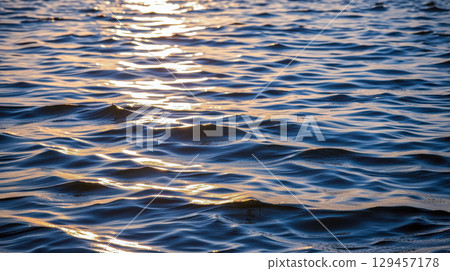 Sunlight reflection on peaceful water surface at sunset with small waves and soft ripples calm evening lake or sea nature texture background 129457178