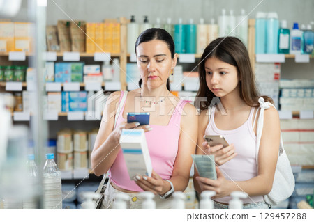 Woman and girl daughter in pharmacy scans QR code on cream 129457288