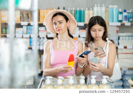 Mom and daughter scanning barcode on sunscreen in chemist's shop Mom and daughter scanning barcode on sunscreen in chemist's shop 129457293