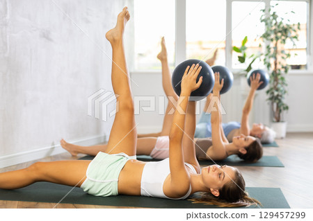 Family grandmother, mother and granddaughter perform fitness exercises lying on floor with softball. Family grandmother, mother and granddaughter perform fitness exercises lying on floor with softball. 129457299