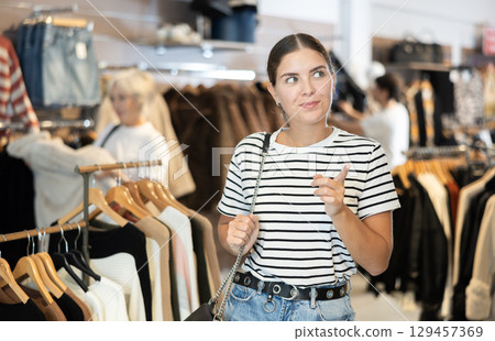 Girl buyer noticed desired product in clothes store and happily smiles from upcoming purchase 129457369