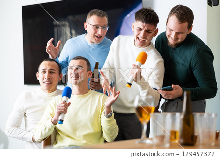 Happy male friends having fun while singing karaoke at a bar. Having fun, celebrating. holiday, leisure, party concept 129457372