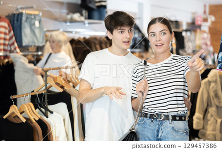Young couple watching excitedly large stock of clothes in clothing store Young couple watching excitedly large stock of clothes in clothing store 129457386