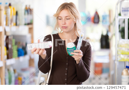 Positive beautiful young woman choosing toothpaste and oral care products in store 129457471
