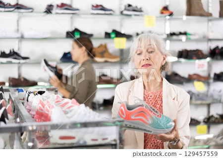 Elderly woman chooses modern sports shoes in shoe store 129457559