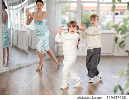 Cheerful tween girl and boy rehearsing jive in dance studio with choreographer 129457668